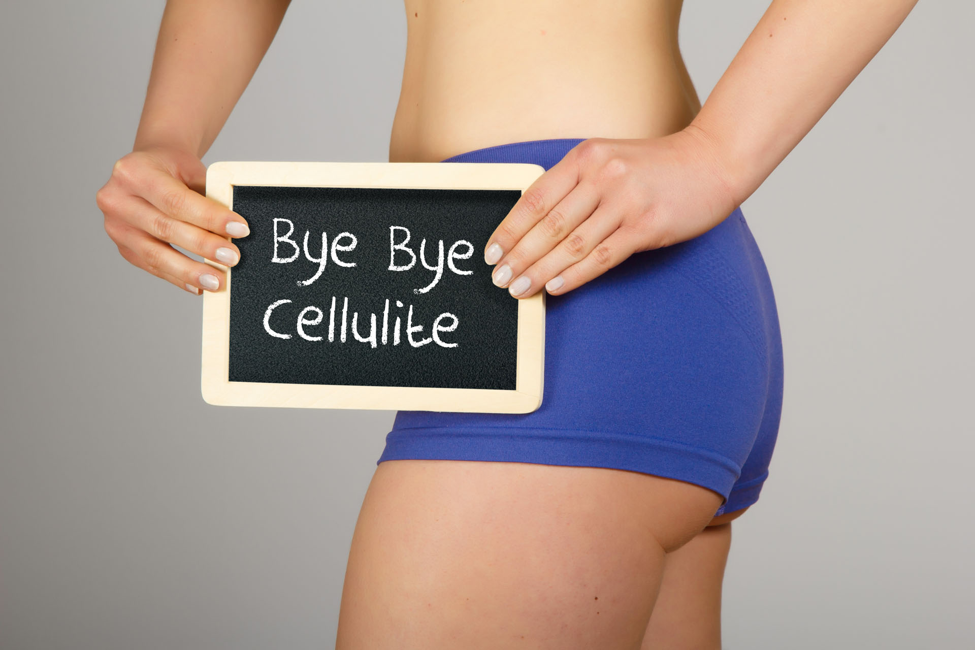 Beautiful young woman in lingerie holding a small chalk board with text "Bye Bye Cellulite" Center focus